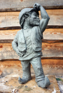 Zdjęcie przedstawiające model rzeźby krasnal budowniczego na tle drewnianej ściany.