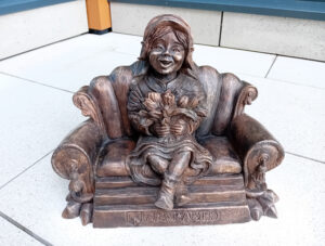 Krasnal dziewczyna, siedzi na zabytkowej sofie i trzyma w ręku bukiet tulipanów.