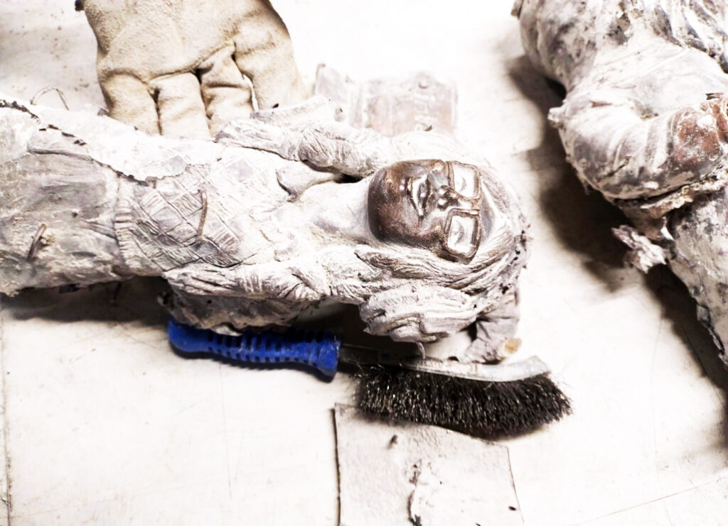 Zdjęcie przedstawia świeżo dwa odlewy z brązu figurek krasnali, są pokryte białym gęstym nalotem, reszkami gipsu i piasku kwarcowego.