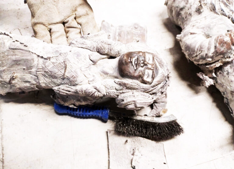 Zdjęcie przedstawia świeżo dwa odlewy z brązu figurek krasnali, są pokryte białym gęstym nalotem, reszkami gipsu i piasku kwarcowego.