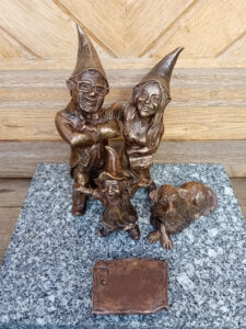 Trzy krasnale obok nich leżący pies, stoją na granitowym postumencie.