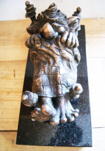 Figurka Trolka leżącego w łóżku, z brązu, na czarnym kamiennym postumencie.